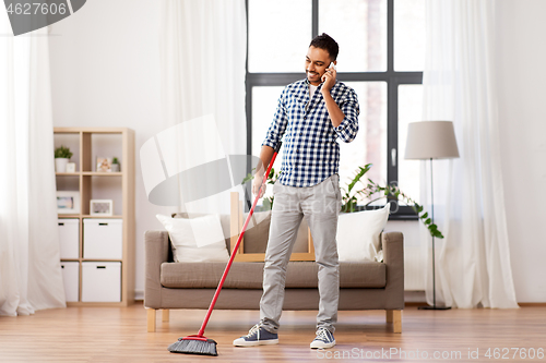 Image of man with broom cleaning and calling on smartphone