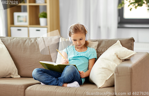 Image of girl in headphones with diary on sofa at home