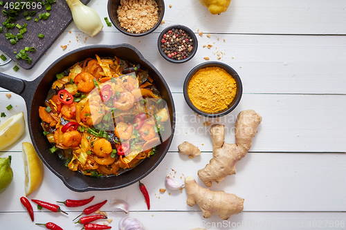 Image of Fresh fried noodles with vegetables with shrimps served in black iron pan. With various ingredients