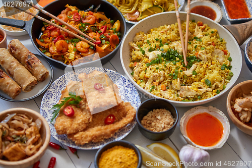 Image of Asian food served. Plates, pans and bowls full of noodles chicken stir fry and vegetables