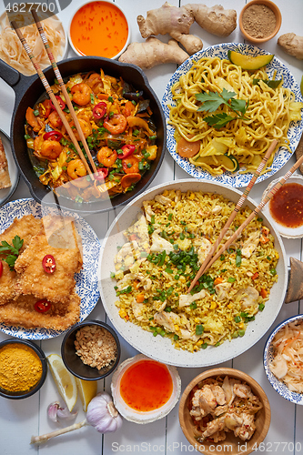 Image of Asian food served. Plates, pans and bowls full of noodles chicken stir fry and vegetables