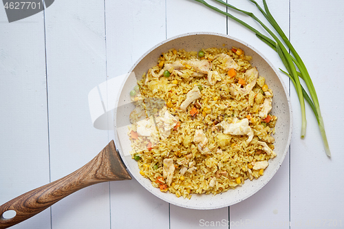 Image of Delicious fried rice with chicken and vegetables served in pan. Placed on white wooden table