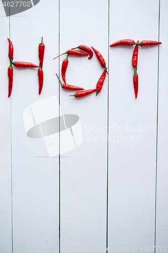 Image of A word HOT formed with small red chilli peppers. Placed on white wooden table