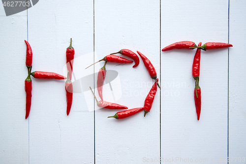 Image of A word HOT formed with small red chilli peppers. Placed on white wooden table