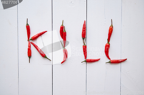 Image of A word KILL formed with small red chilli peppers. Placed on white wooden table