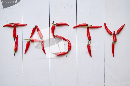 Image of A word TASTY formed with small red chilli peppers. Placed on white wooden table