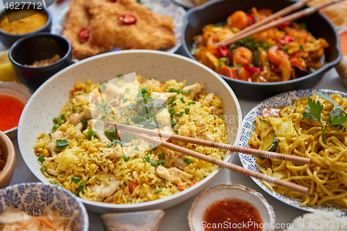 Image of Asian food served. Plates, pans and bowls full of noodles chicken stir fry and vegetables