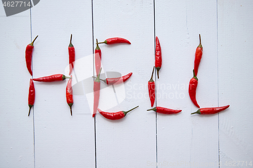 Image of A word HELL formed with small red chilli peppers. Placed on white wooden table