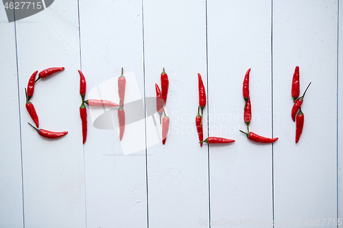 Image of A word CHILLI formed with small red chilli peppers. Placed on white wooden table