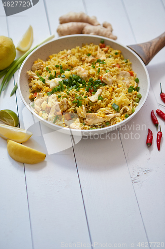 Image of Delicious fried rice with chicken and vegetables served in pan. Placed on white wooden table