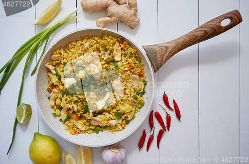 Image of Delicious fried rice with chicken and vegetables served in pan. Placed on white wooden table
