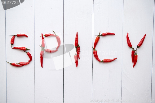 Image of A word SPICY formed with small red chilli peppers. Placed on white wooden table