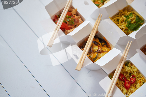 Image of Various oriental dishes packed in paper box. Food is delivered on the table. Asian take away concept