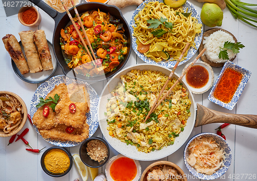 Image of Asian food served. Plates, pans and bowls full of noodles chicken stir fry and vegetables