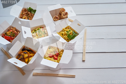 Image of Various oriental dishes packed in paper box. Food is delivered on the table. Asian take away concept