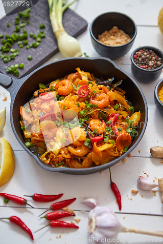 Image of Fresh fried noodles with vegetables with shrimps served in black iron pan. With various ingredients