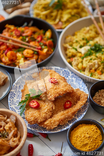 Image of Asian food served. Plates, pans and bowls full of noodles chicken stir fry and vegetables