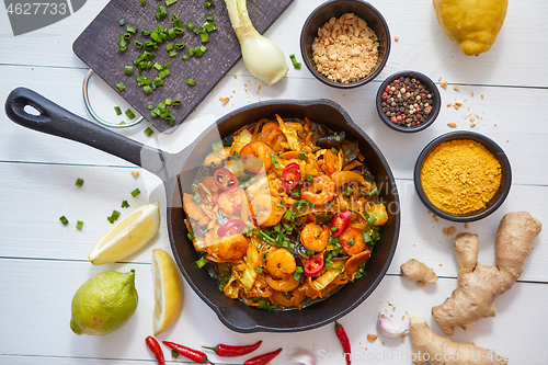 Image of Fresh fried noodles with vegetables with shrimps served in black iron pan. With various ingredients