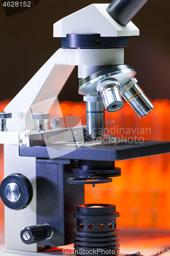 Image of Close up of microscope lenses focused on a specimen in warm orange light light.