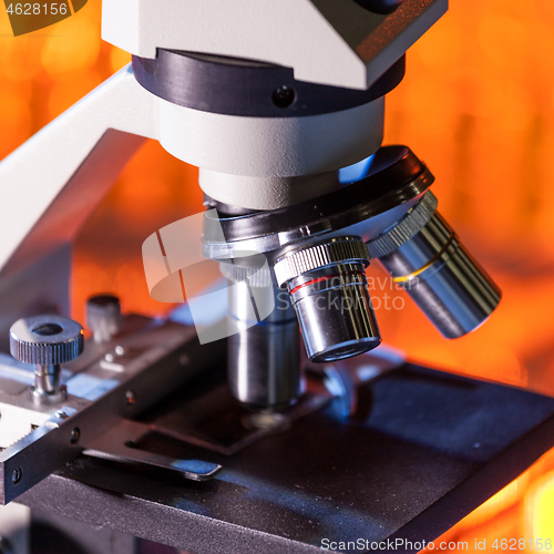 Image of Close up of microscope lenses focused on a specimen in warm orange light light.