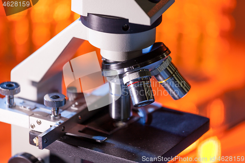 Image of Close up of microscope lenses focused on a specimen in warm orange light light.