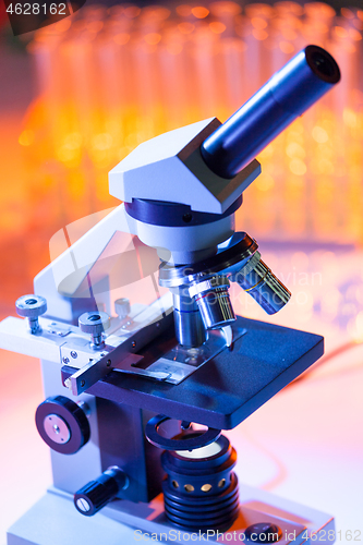 Image of Close up of microscope lenses focused on a specimen in warm orange light light.