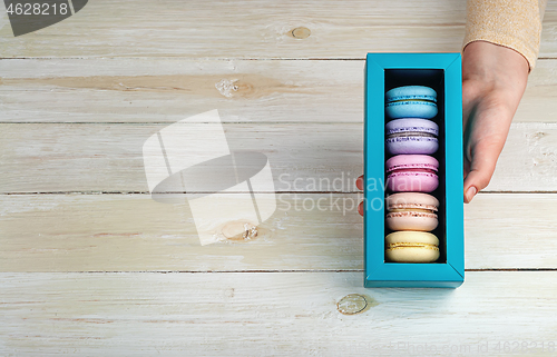 Image of Female hand holds gift box with macaroons