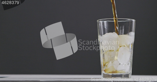 Image of In a glass with ice pour coffee with splashes and bulbaki around dark background.