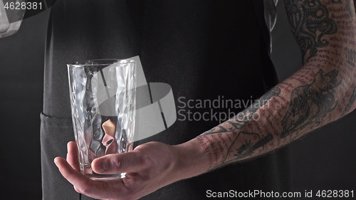 Image of A man with a tattoo is pouring ice cubes into a glass around a dark background. 4K UHD video, 2160p.