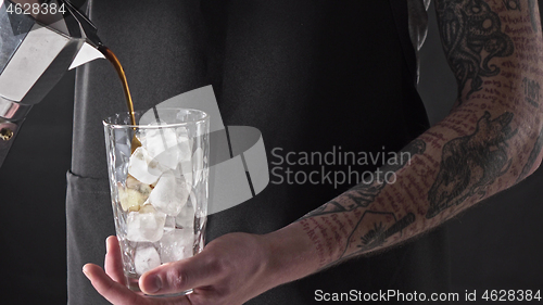 Image of A man with a tattoo pours coffee in a glass with ice around a dark background. 4K UHD video, 2160p.