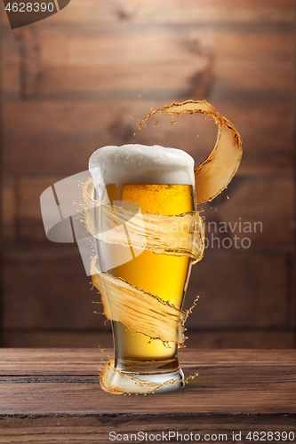 Image of Glass of light fresh beer with flying spiral splash around mug.