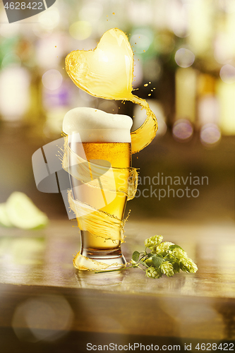 Image of Flying heart splash of light beer above glass of fresh beverage.