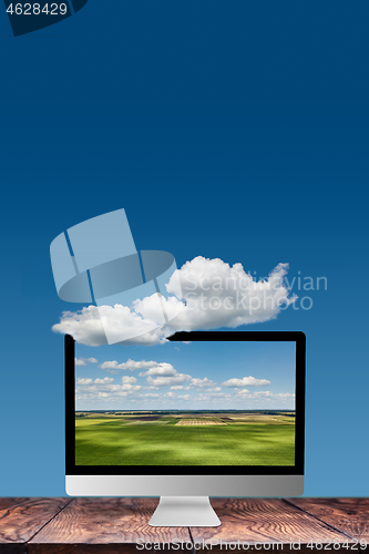 Image of Monitor with landscape on a wooden table and blue sky background.