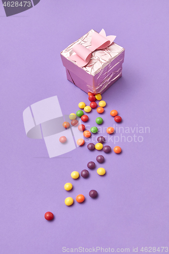 Image of A ripped gift box with colorful candy on a purple background.