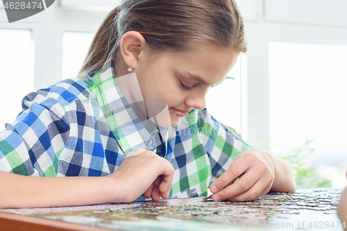 Image of Passionate girl collects puzzles at home at the table