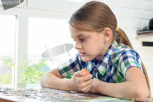 Image of Girl collects a puzzle while sitting at home at the table and eats carrots