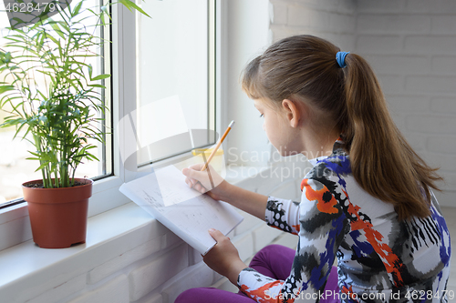 Image of A teenager draws with a pencil in an album sitting on the floor in front of the window