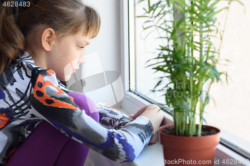 Image of Upset girl sitting by the window and looking very sad out the window