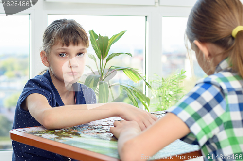 Image of Sad girl collects puzzles in the company of girlfriends and looked into the frame