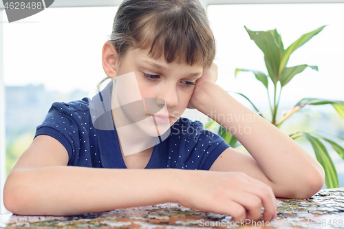 Image of Tired girl collects puzzle for a long time