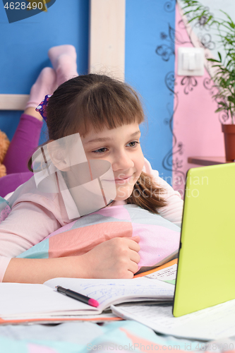 Image of The girl is remotely studying at home, lying in bed and watching a video lesson