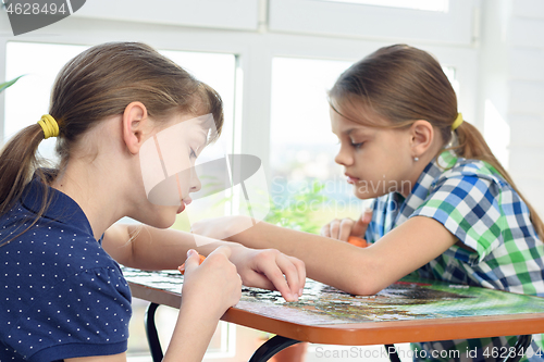 Image of Two girls enthusiastically collect puzzles at the table at home