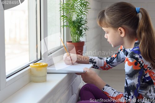 Image of The child draws with a pencil on the windowsill at home