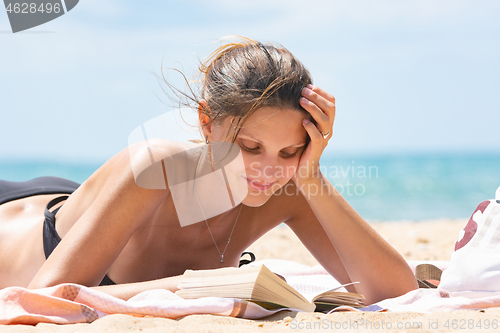 Image of Girl in swimsuit reads book lying on sandy beach near the sea