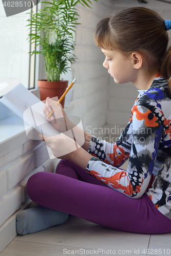 Image of Passionate girl at home paints a landscape sitting on the floor by the window