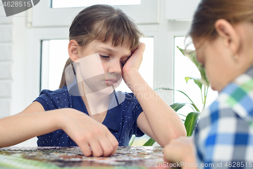 Image of Tired girl reluctantly collects jigsaw puzzles with her friend