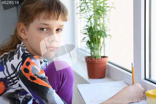 Image of Girl spending time at home in quarantine, girl draws while sitting by the window