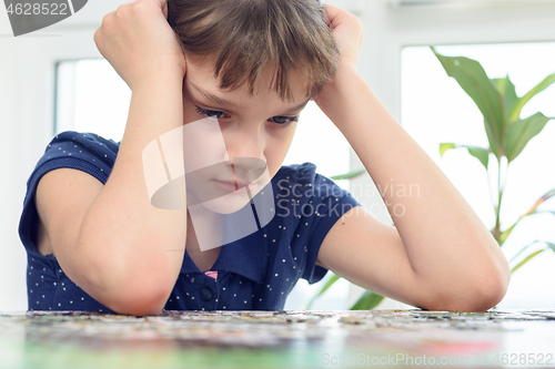 Image of Girl thinking over a puzzle while sitting at home at the table