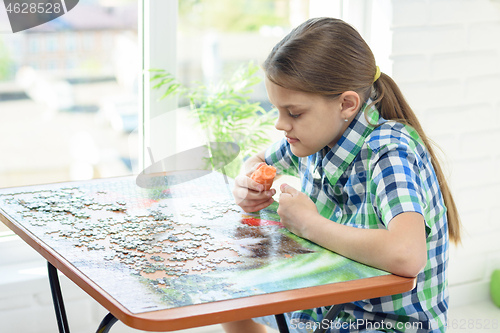 Image of Girl at home by the window collects puzzles on his day off