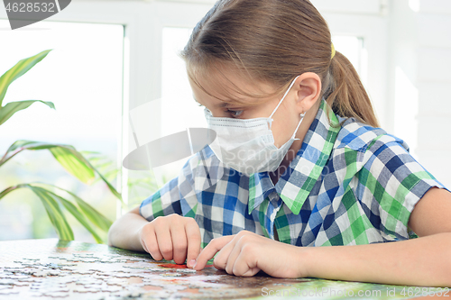 Image of Teen girl in a medical mask collects a puzzle in a detention center